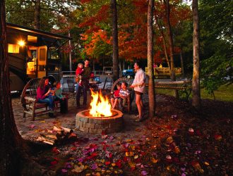 Family around a campfire with an RV in the background