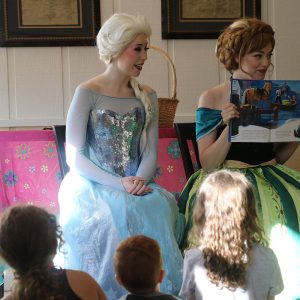 women dressed as Frozen sisters reading to children