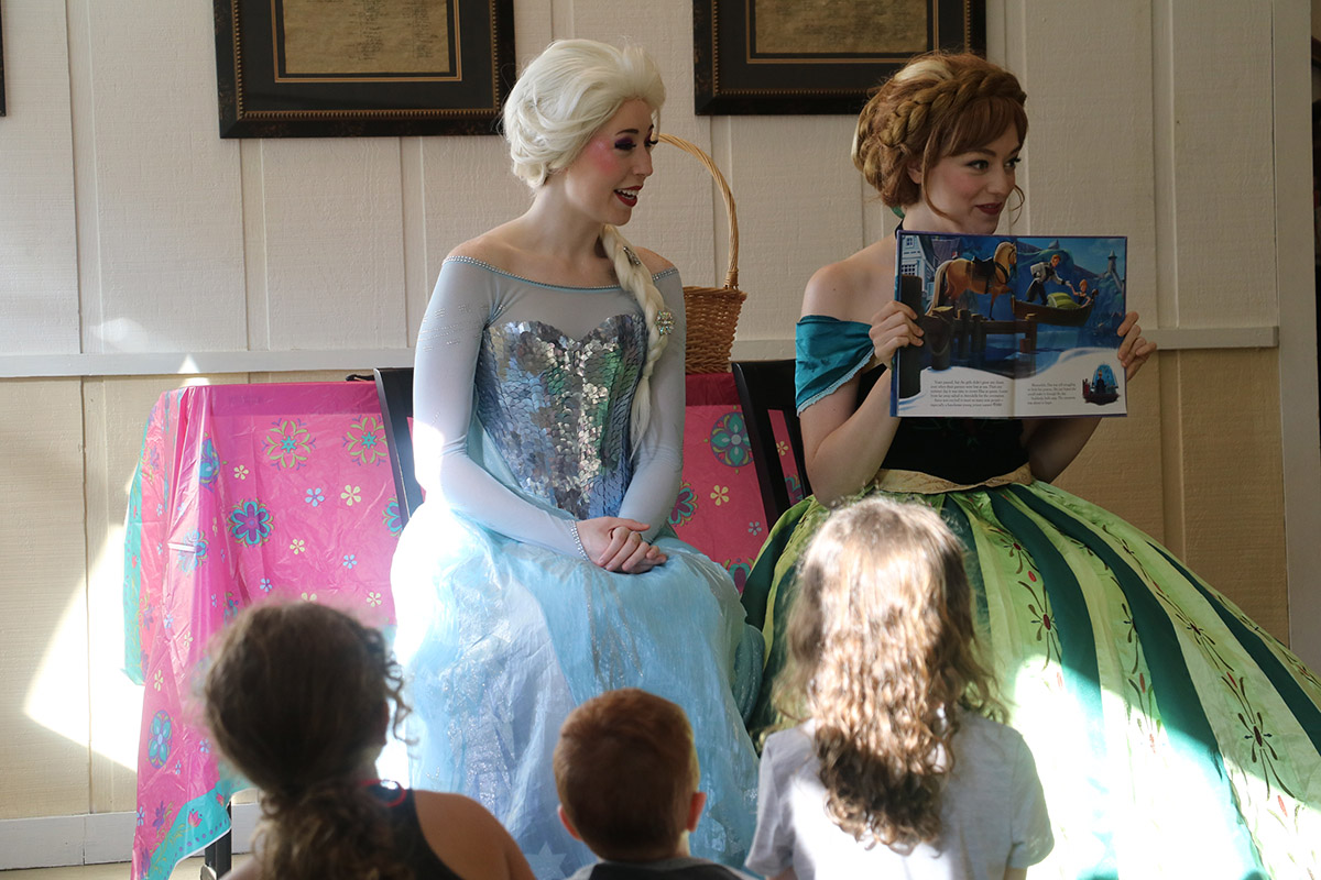women dressed as Frozen sisters reading to children