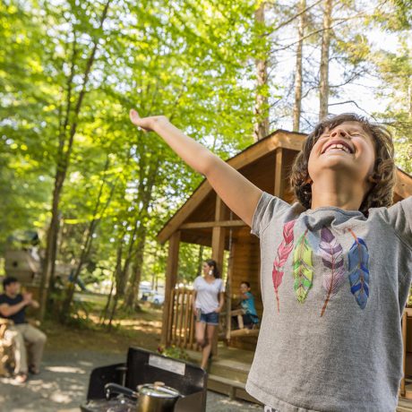 kid smiling with arms outstretched in front of cabin