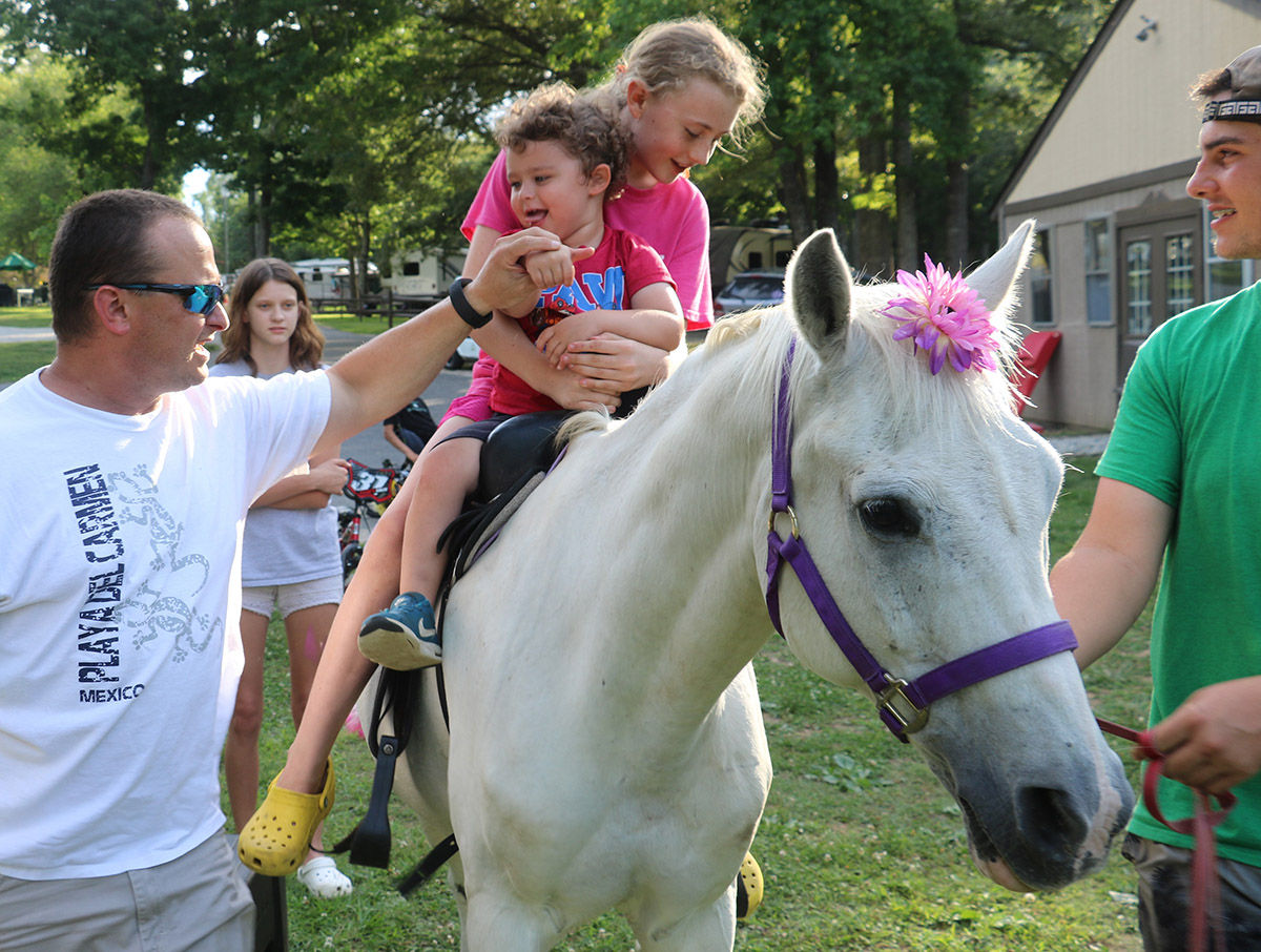 father holding kid's hand while children ride a horse
